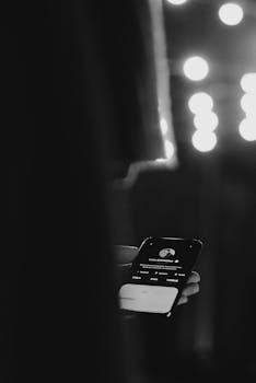 A black and white image showing a hand holding a smartphone with a user profile interface, highlighting mobile technology.