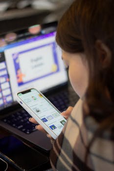 A young woman using a smartphone and laptop, engaged in digital learning indoors.