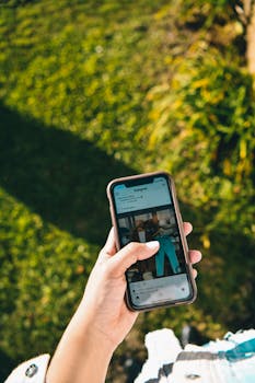 Close-up of a person's hand holding a smartphone with social media on screen outdoors.