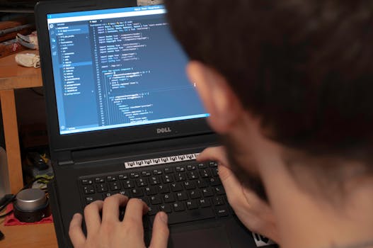 Close-up view of a programmer typing code on a laptop in a workspace.