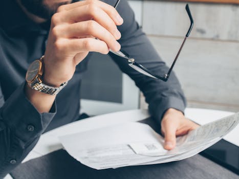 Man in formal attire reviewing paperwork, holding glasses. Business setting.