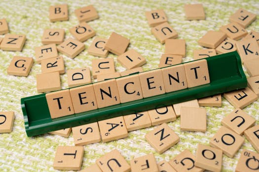 Wooden Scrabble tiles arranged to spell 'Tencent' on a green tile holder, scattered letters in the background.