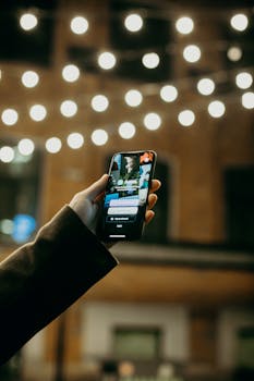 A hand holding a smartphone in a city at night, with blurred street lights.