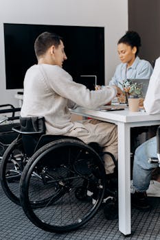 Office scene with diverse colleagues collaborating, including person in wheelchair.