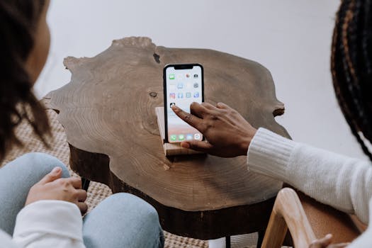 Two individuals use a smartphone together indoors, focused on screen interaction on a wooden table.