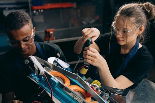 Two students working together on building a robot in an industrial setting, wearing protective goggles.