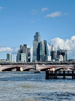 A clear day view of modern skyscrapers behind a bridge over the Thames River, London.