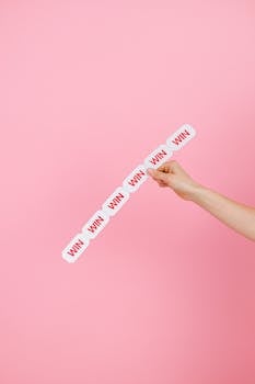 Conceptual image of a hand holding 'WIN' labels against pink background.