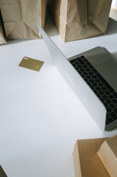 A laptop with a credit card, surrounded by paper bags, illustrating online shopping.