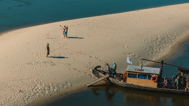 A scenic aerial view of people enjoying a sandy beach next to a wooden boat in Warsaw, Poland.