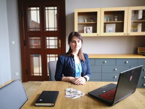 Caucasian woman using laptop at desk in modern office setting with natural light.