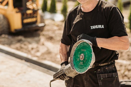 Male construction worker in protective gear using a circular saw outdoors on a sunny day.